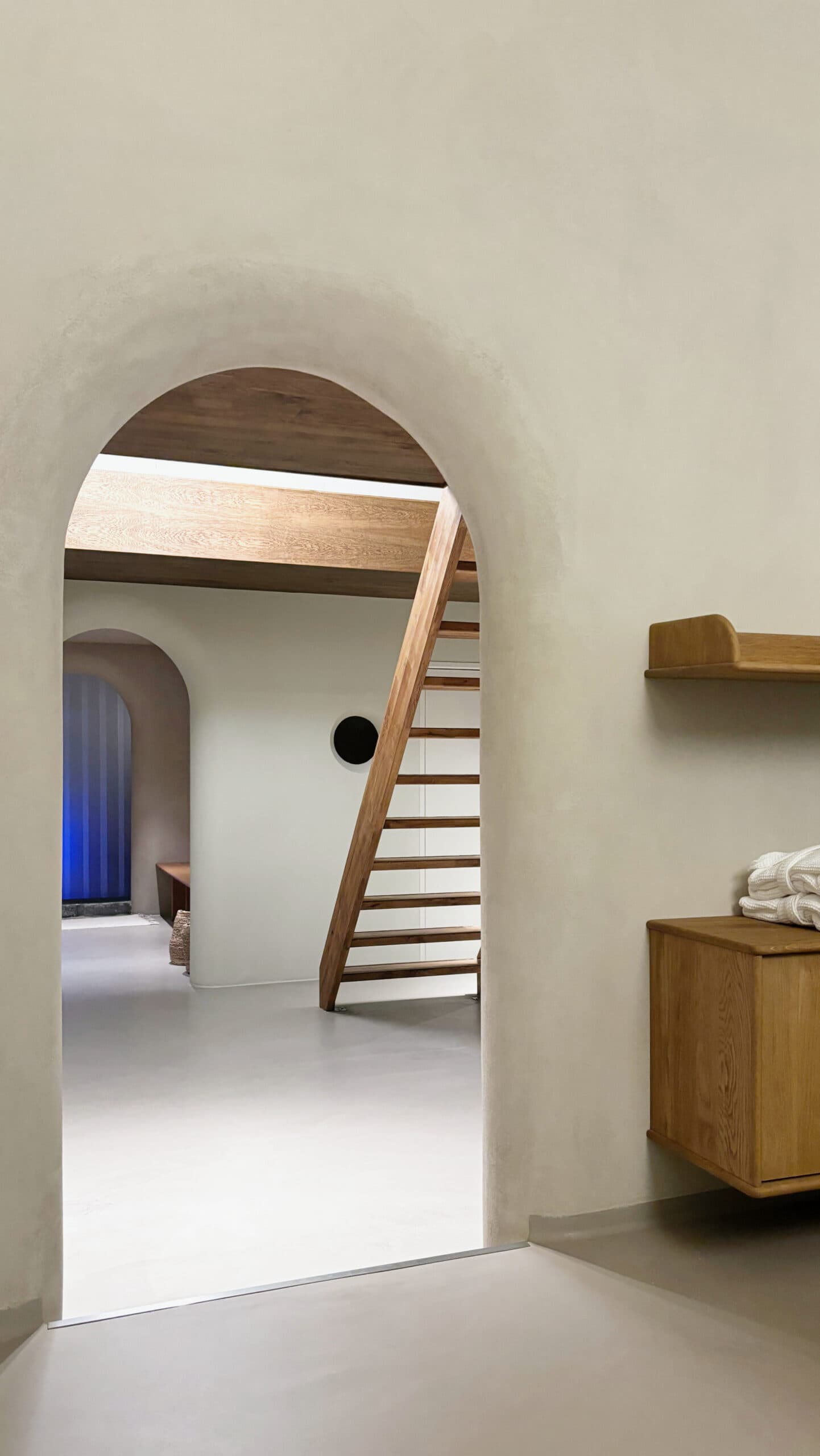 Arched doorway framing staircase with oak shelving and towels